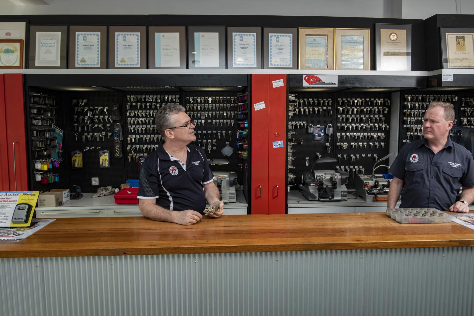 Two locksmith staff behind a service counter with key displays and certificates on the wall