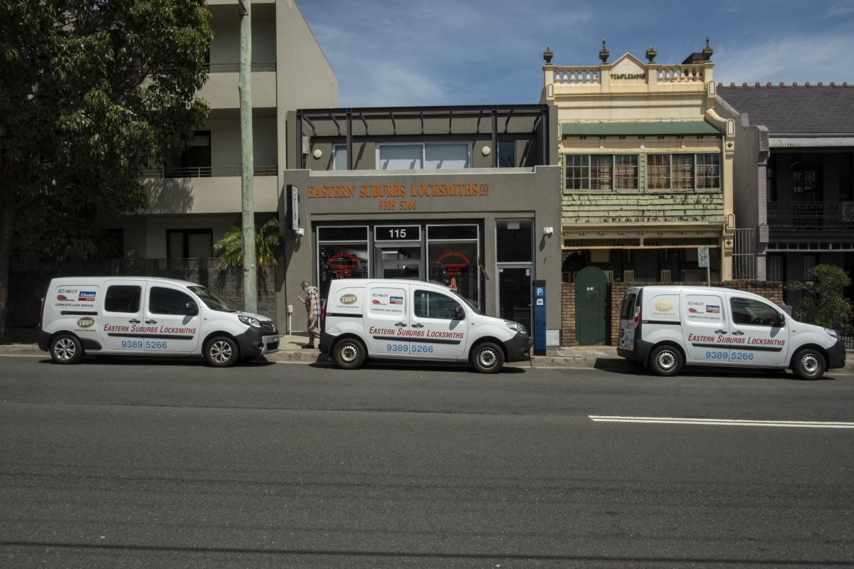 Three mobile locksmith vans parked outside shops on a city street