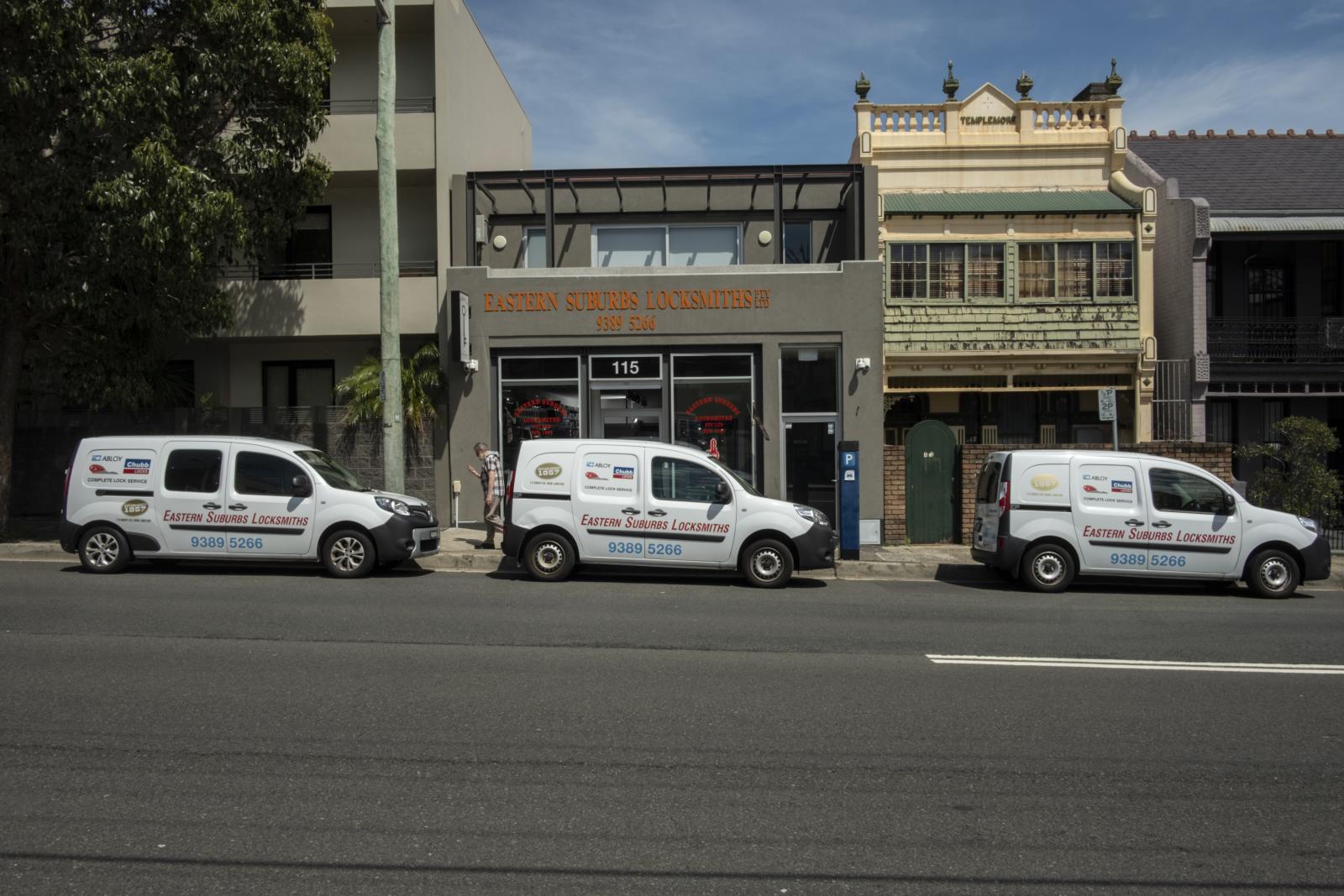 Three mobile locksmith vans parked outside shops on a city street