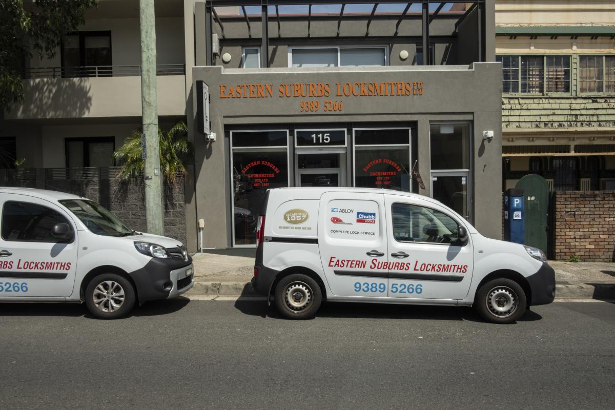 Two mobile locksmith vans parked outside an Acme Locksmiths shopfront on a city street