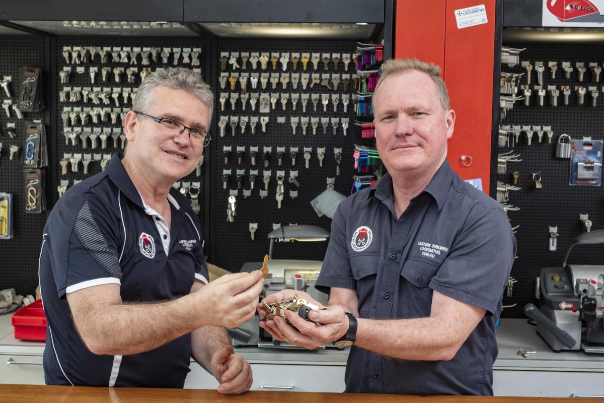 Two locksmiths in a key cutting shop holding a set of keys at the service counter