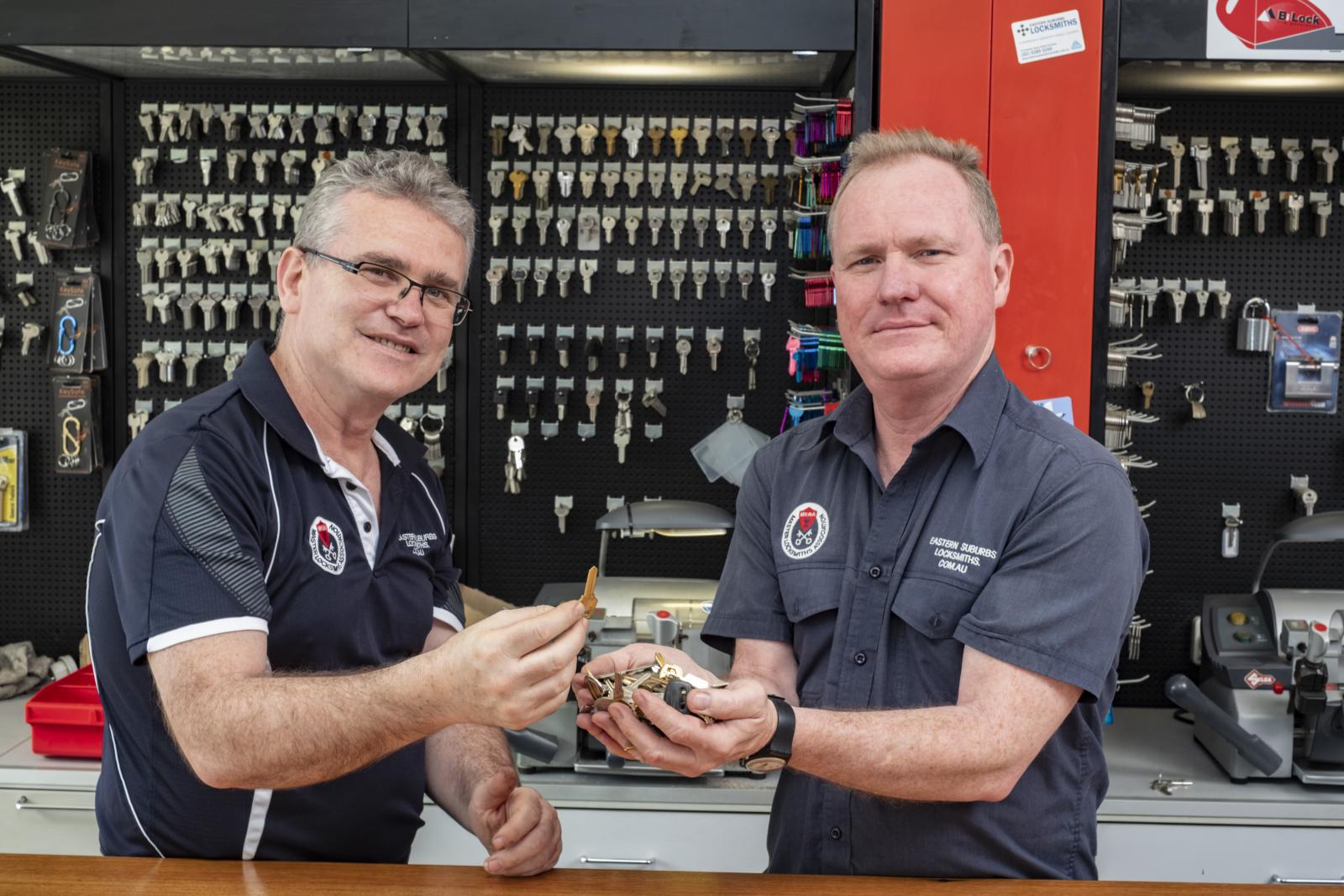 Two locksmiths in a key cutting shop holding a set of keys at the service counter