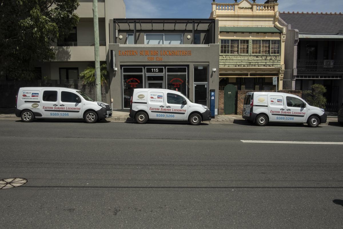 Three branded locksmith vans parked outside commercial premises on a city street