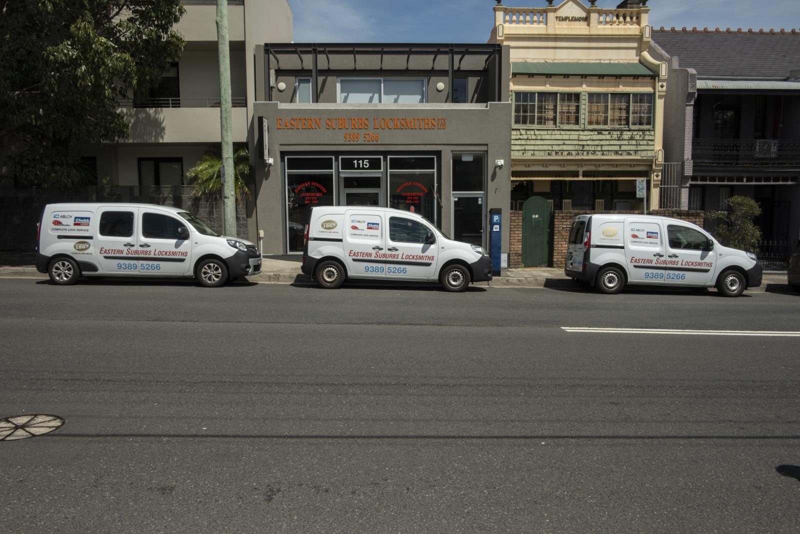 Three branded locksmith vans parked outside commercial premises on a city street