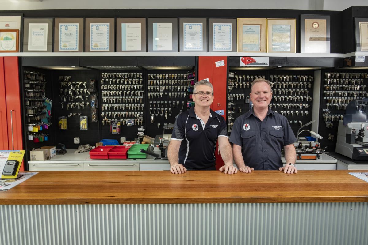 Two locksmith staff behind a counter with key boards and certificates in the background