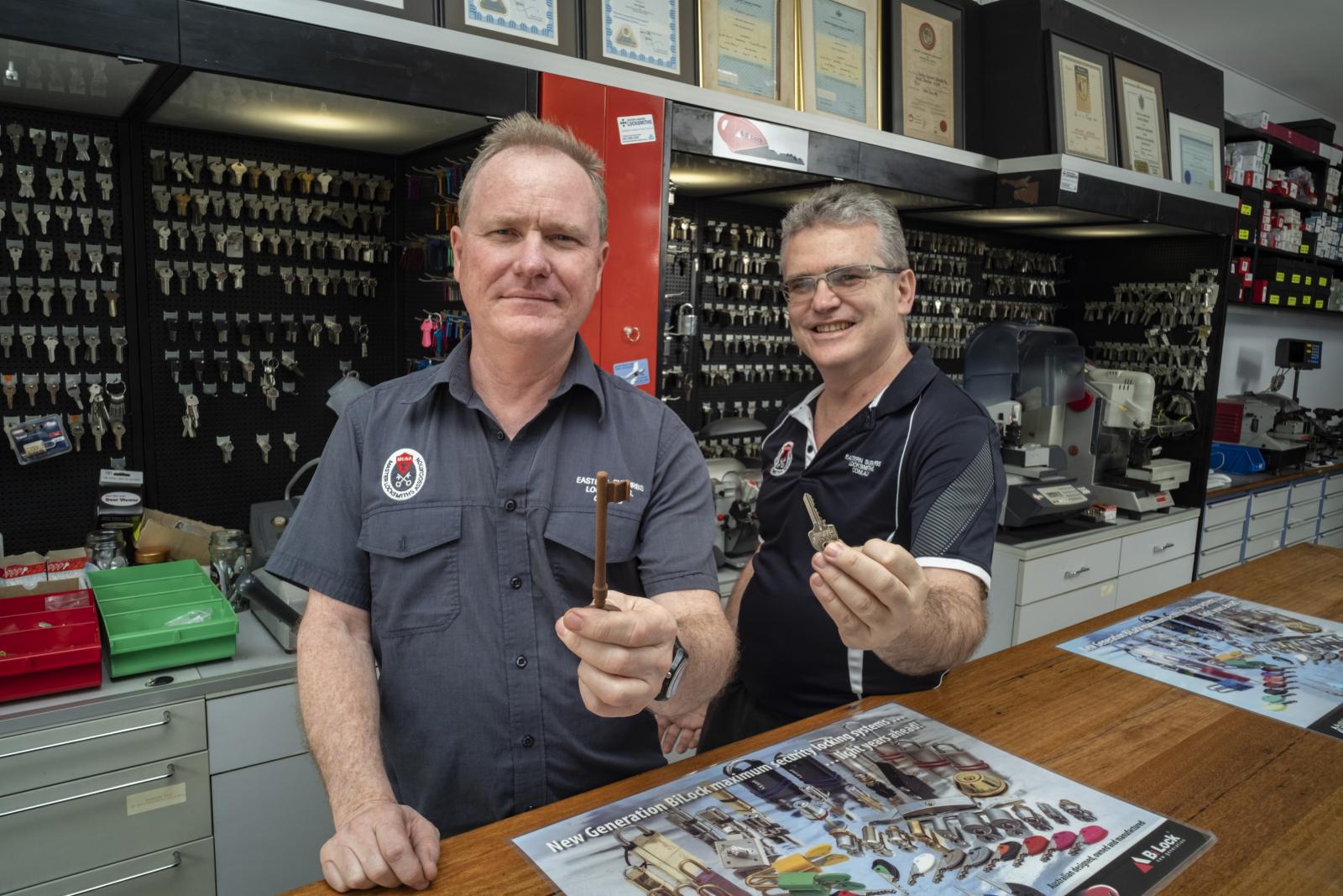 Two locksmiths in a key cutting shop holding keys at the service counter
