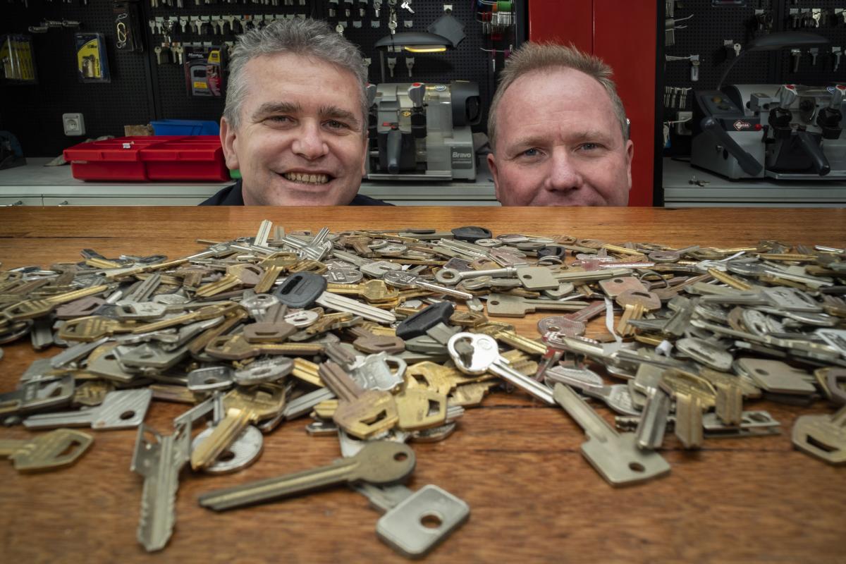 Two locksmiths behind a counter covered with assorted keys