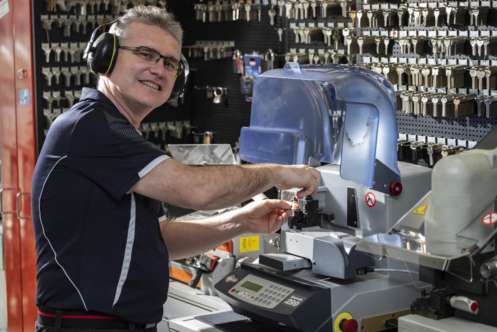 Locksmith operating a key cutting machine in a workshop with keys on display