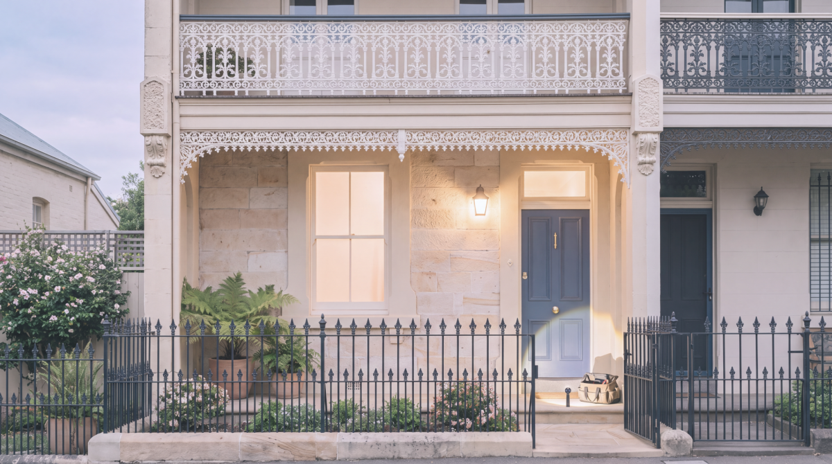 Front entrance of a terrace home with a blue door, iron fence and exterior lighting