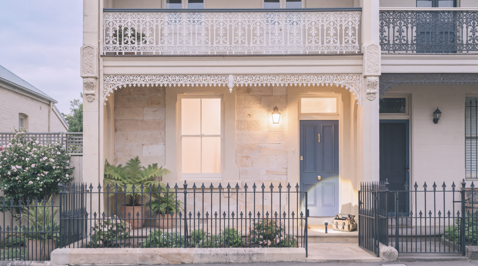 Front entrance of a terrace home with a blue door, iron fence and exterior lighting