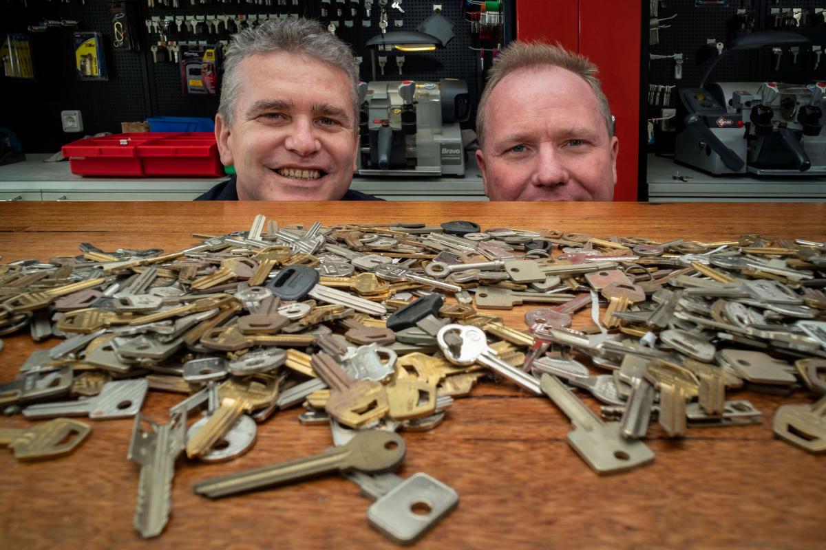 Two locksmiths behind a workbench covered with assorted keys in a key cutting shop